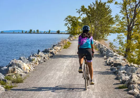 Woman riding a bike on a gravel road, surrounded by a large lake