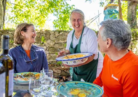 Man and woman smiling at a dinner table with a woman holding a large bowl of food
