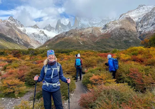 Woman smiling while holding hiking poles, with large mountains in the background