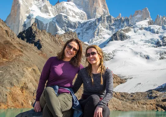 Two women smiling while sitting on boulders in front of a lake