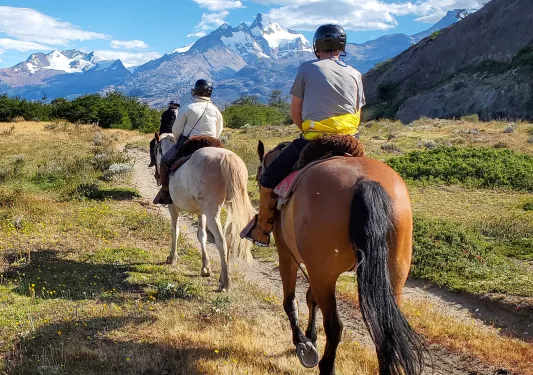 Three people horseback riding on a dirt trail in the middle of an open valley