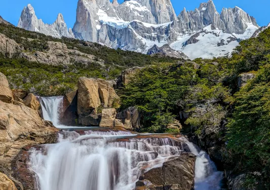 Active waterfall on large boulders with tall mountains in the background