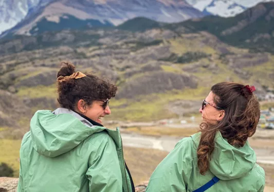 Two women wearing green jackets, smiling while looking towards an open valley