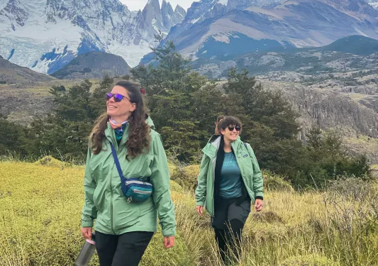 Two women smiling while walking in a field with tall weeds