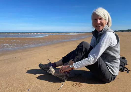 Woman sitting on the beach, untying her hiking shoes