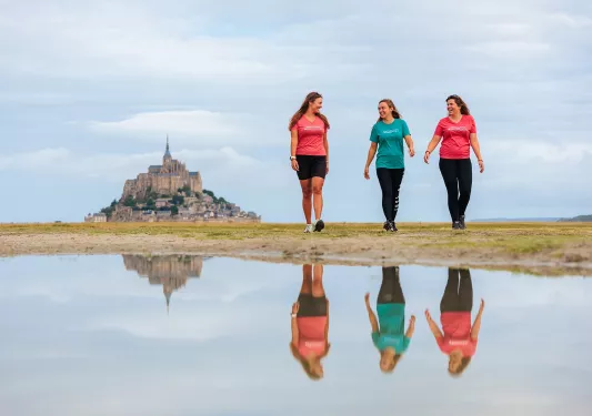 Three women walking on an empty valley, with a large castle in the distance