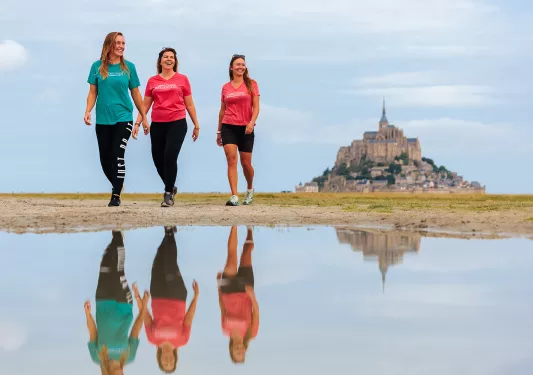 Three woman walking on a sandy path, with a puddle showing their reflection