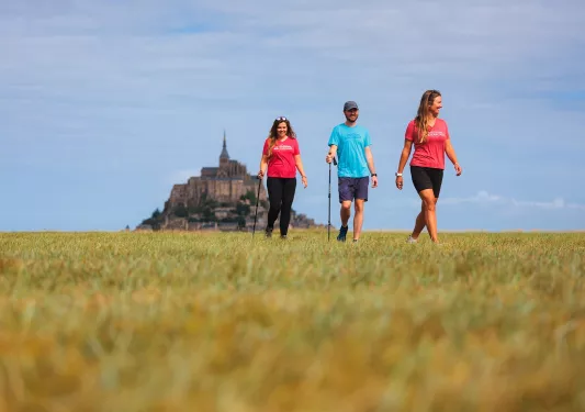 Two women and one man walking on an empty field, with a large castle in the distance
