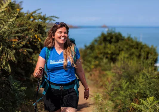 Woman smiling while walking on a dirt trail surrounded by thick plants