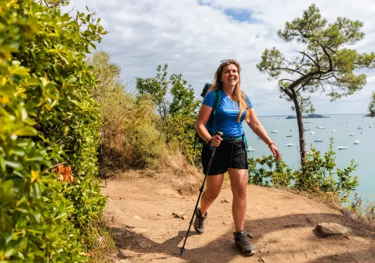 Woman walking on a dirt trail with the ocean in the background