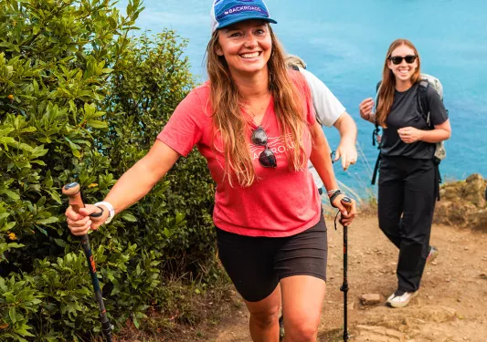 Two women with walking poles ascending a sandy path