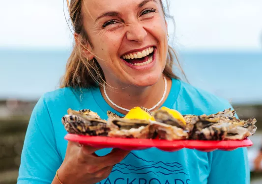 Woman smiling and holding a red plate full of oysters