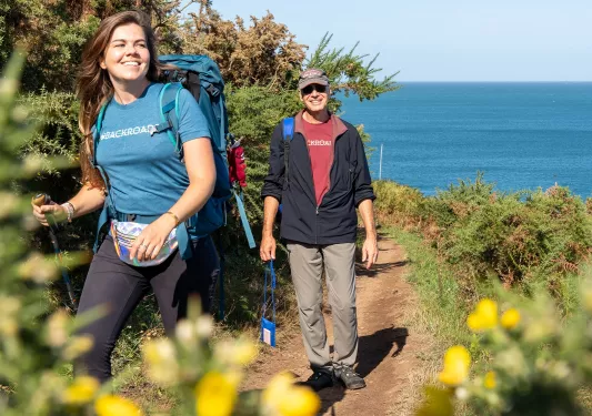 Man and woman walking on a dirt trail, smiling with the ocean in the distance