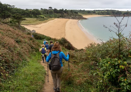 Group of people descending a dirt trail on a hill towards a beach