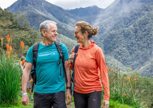 Man and woman walking on a dirt trail, with hills in the background