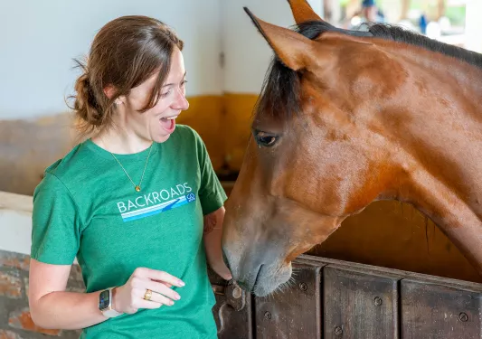 Woman in a green shirt, smiling while petting a horse