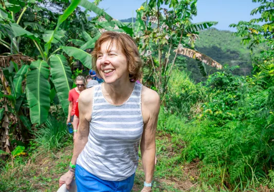 Woman smiling while ascending a trail surrounded by tall plants
