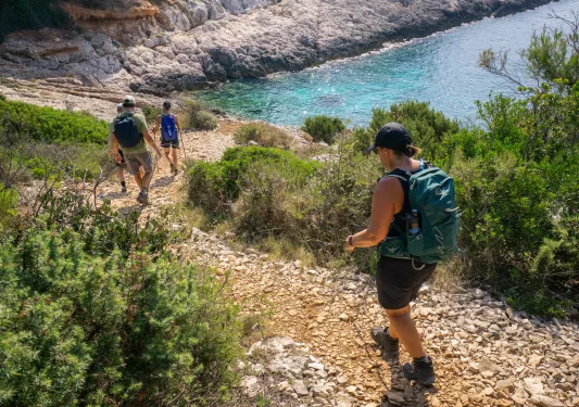 Men and women descending a rocky trail, towards a body of water