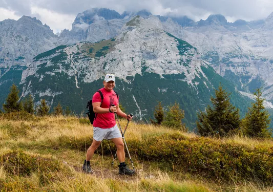 Man in red shirt hiking on a dirt trail with snow-capped mountains in the background