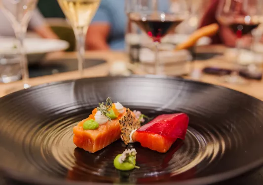 Black plate with prepared, raw fish and wine glasses in the background