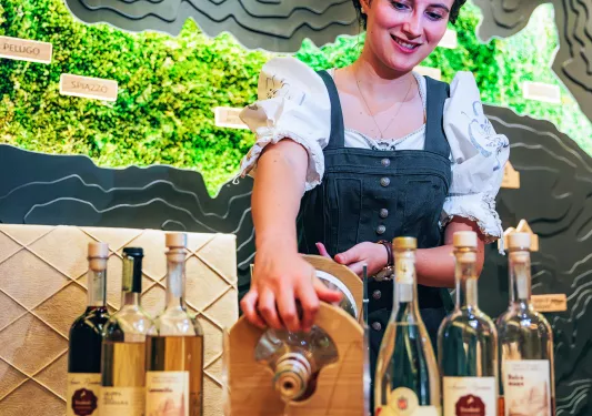 Woman pouring alcohol into a glass, surrounded by other bottles of alcohol