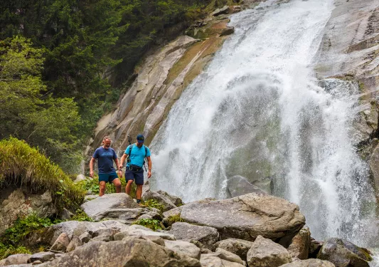 Two men hiking on a rocky trail next to a waterfall