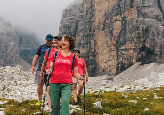 Three women and one man hiking on a grassy trail with fog-covered mountains in the background