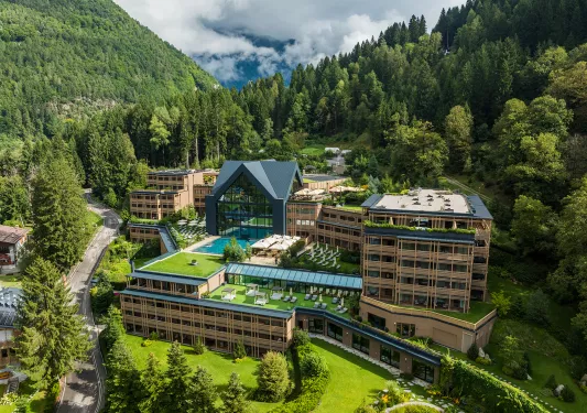 Exterior view of a large hotel complex surrounded by tall trees and hills in the background