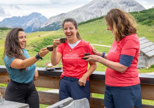 Three women smiling while raising small cups of coffee