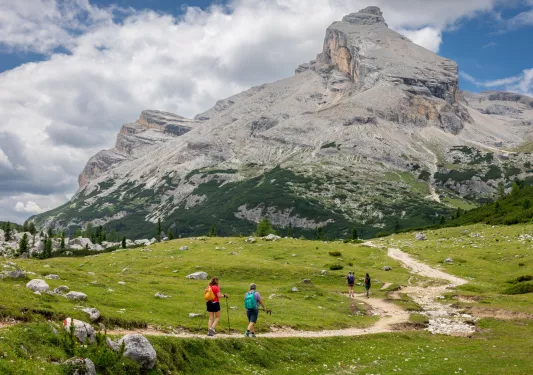 Group of people hiking on a dirt trail, towards a large mountain
