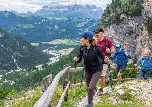 Group of men and women with hiking poles, walking on a dirt trail looking out towards a valley