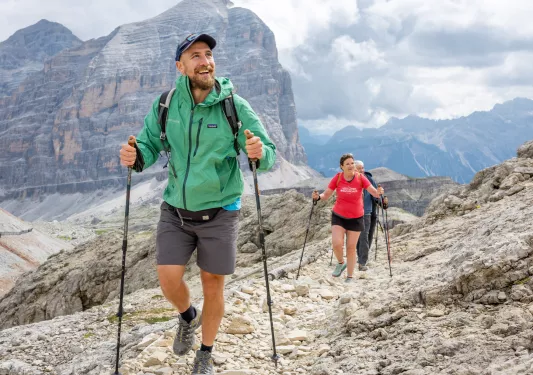 Man and woman with hiking poles, walking on a rocky trail on a mountain