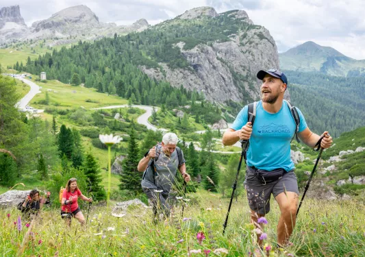 Group of men and women hiking up a grassy hill, with large valleys in the distance