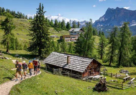 Wooden cabin with a group of people hiking to the left