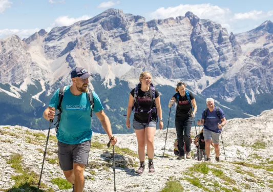 Group of men and women hiking on a rocky trail, with tall mountains in the distance