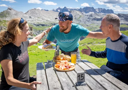 Two men and one woman smiling while being served a plate of bread and cured meats