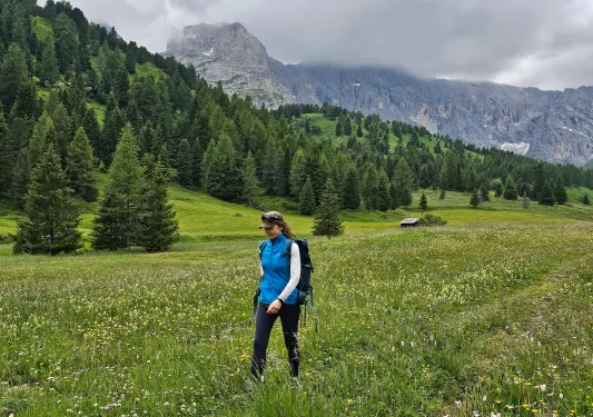 Woman walking through a grassy valley with a forest in the background