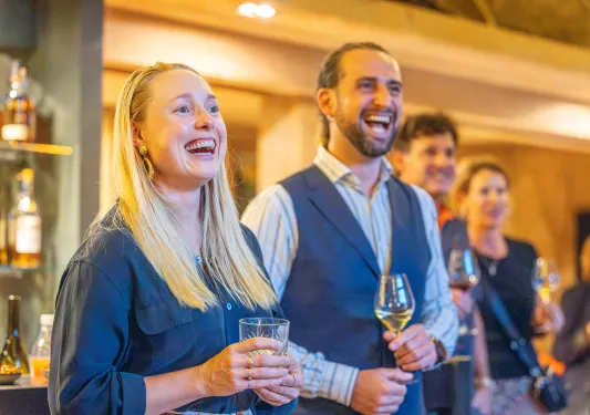 Group of men and women smiling while holding glasses of wine and spirits