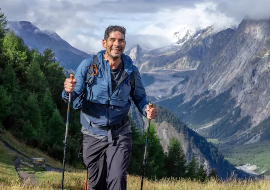 Man with hiking poles, walking on a grassy valley while smiling
