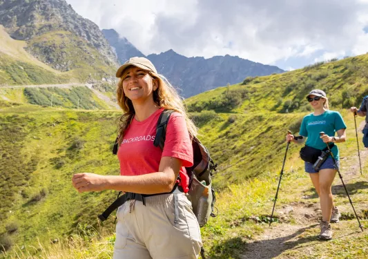 Two women smiling while walking on a dirt and grass trail