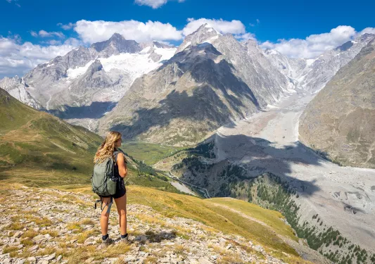 Woman wearing a backpack, looking out to a large valley of mountains and trees