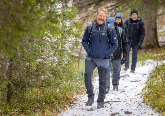 Group of people hiking along a snowy trail, with trees to the left