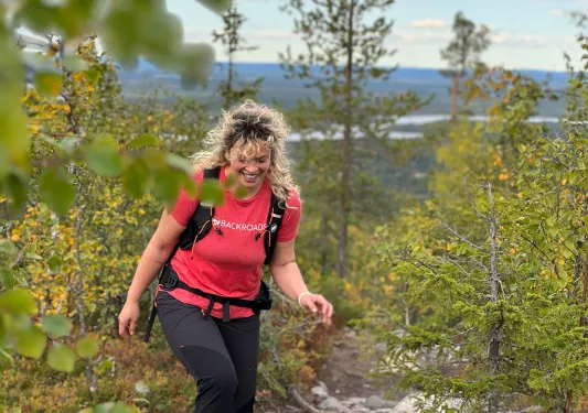 Woman in a red Backroads shirt, ascending a rocky hill surrounded by plants