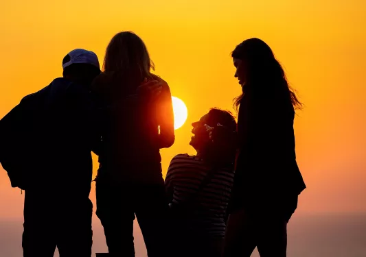 Group of people standing next to each other and laughing, with the sunset in the distance