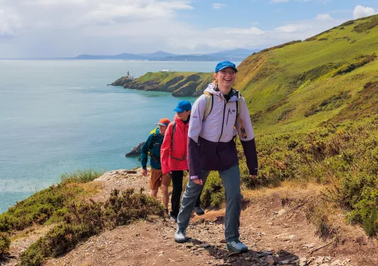 Group of people walking on a dirt trail on a hill, with the ocean in the distance