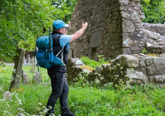 Man wearing a backpack, with both arms pointed out towards ruins
