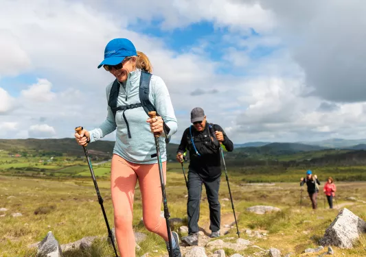 Man and woman with hiking poles, walking on a rocky, grass trail