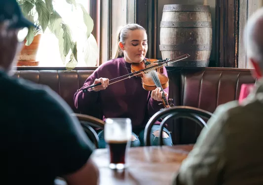 Woman playing the violin in a lounge with a group of people watching