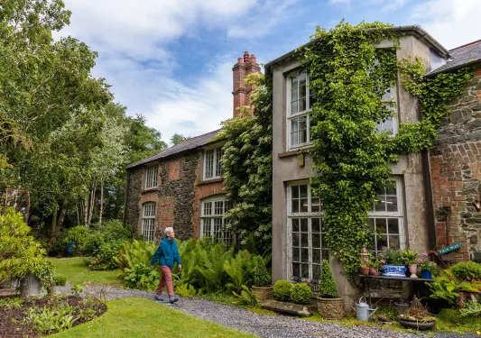 Woman walking next to a large, brick building with large windows and tall plants