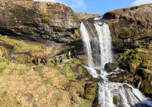Group of people hiking on a hill with a waterfall over the hill